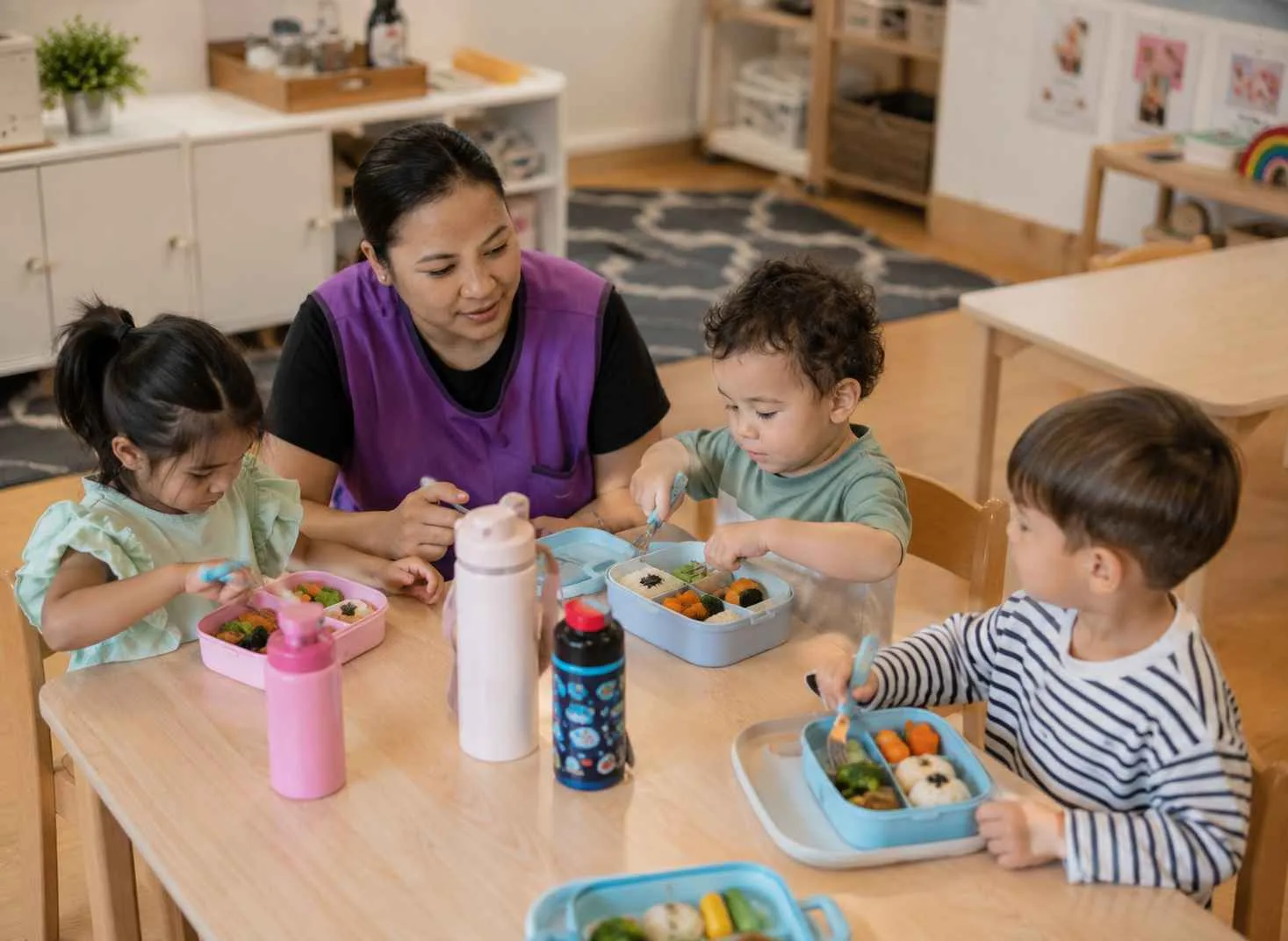 Teacher sitting with children during snack time at nursery