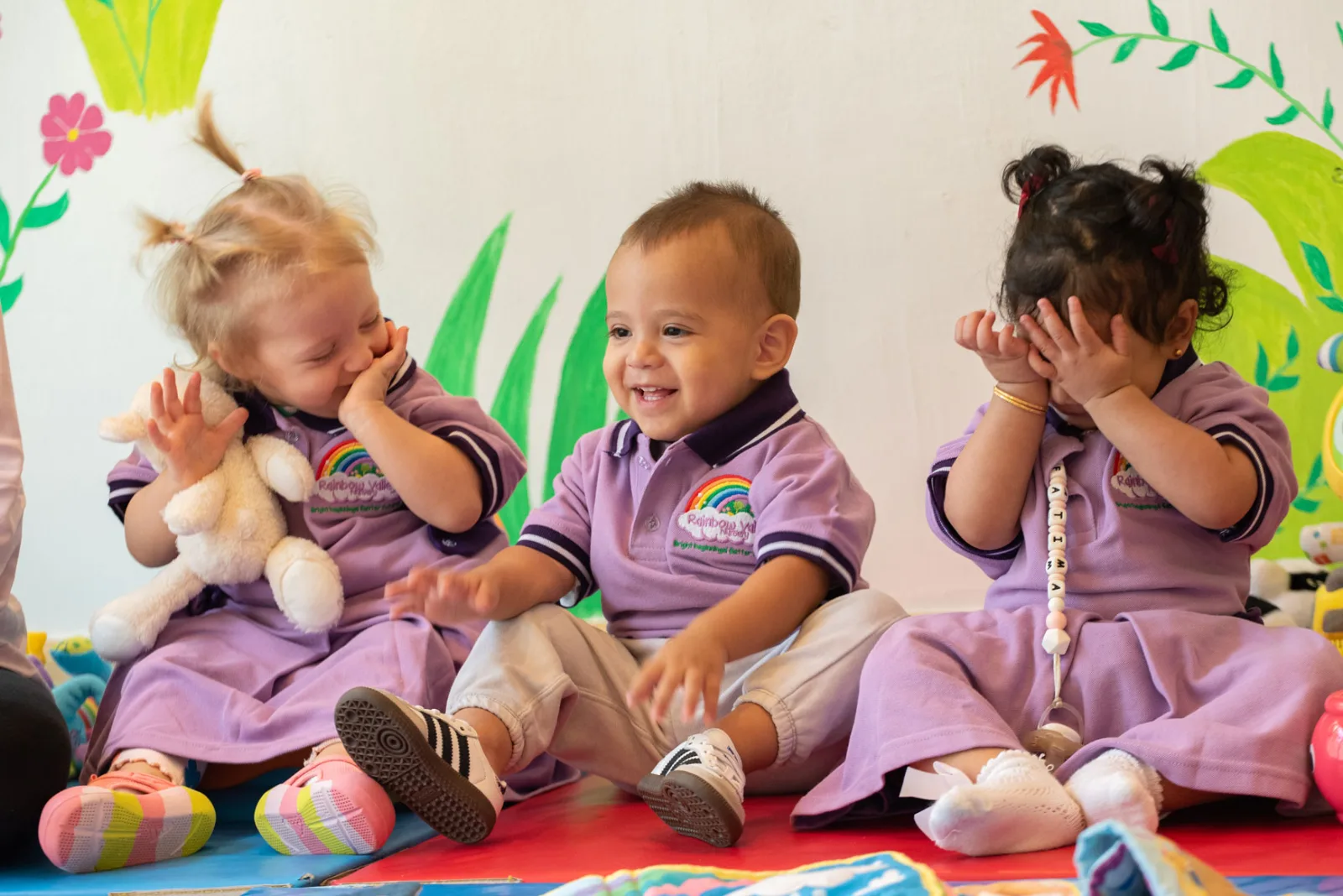 Three toddlers in Rainbow Valley Nursery uniform sitting on the floor