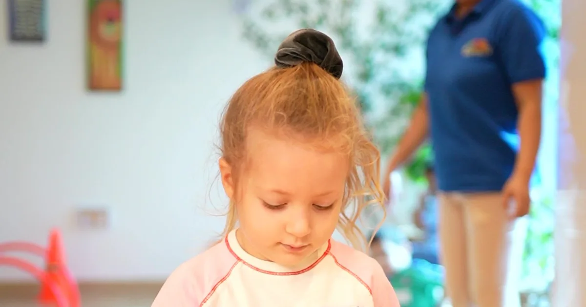 A child exploring the Rainbow Valley Nursery classroom while a teacher looks on